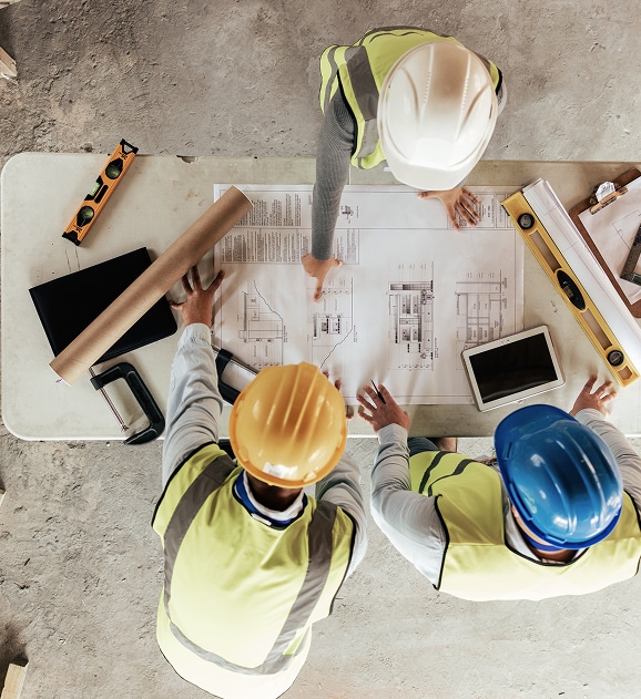 Plan de Construction : Ingénieurs en réunion de chantier Ingénieurs en gilet de sécurité analysant un plan de construction sur un chantier avec divers outils de mesure.
