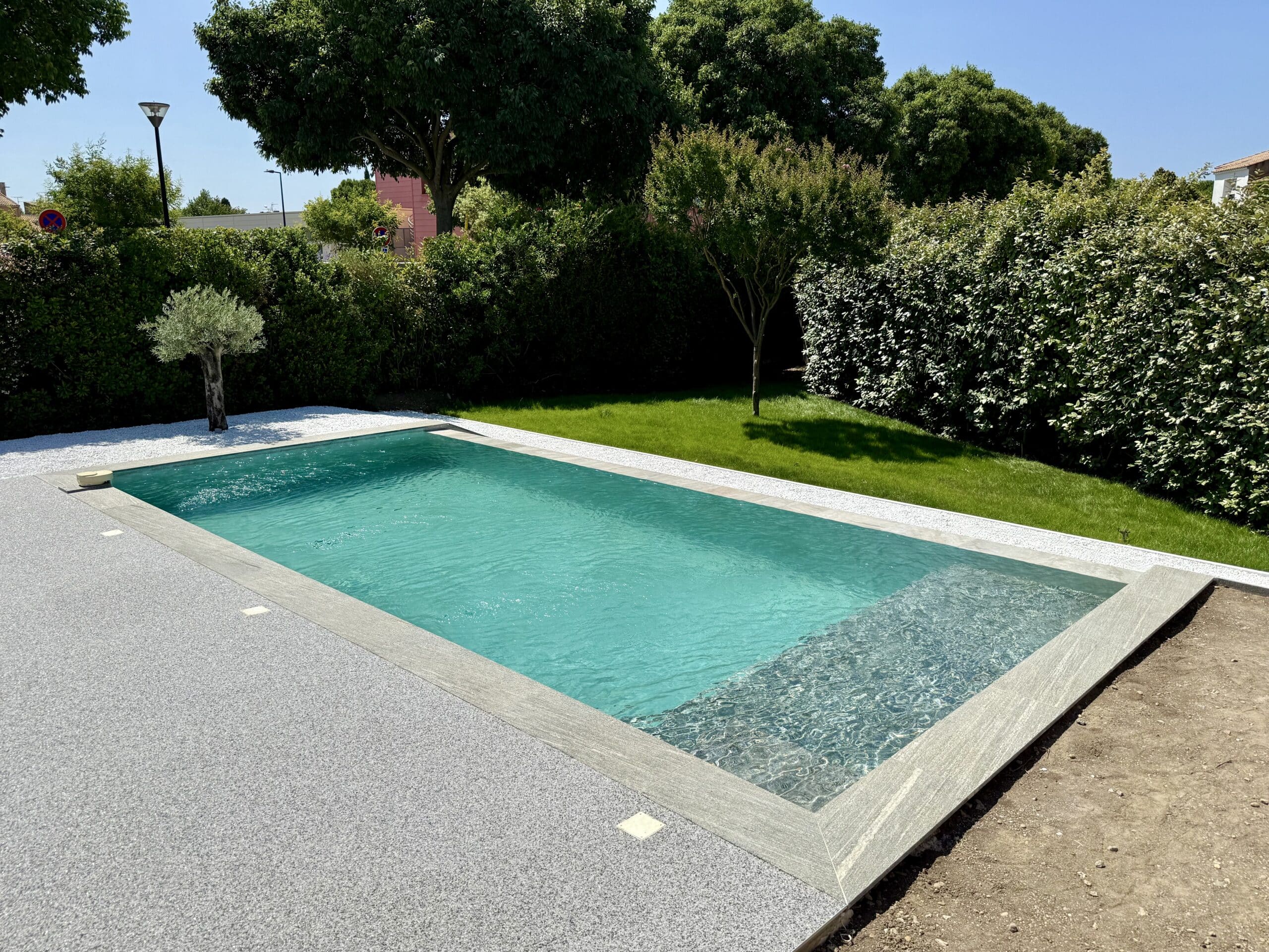 Piscine Moderne avec Eau Turquoise et Jardin Paysager Piscine rectangulaire moderne à l'eau turquoise avec terrasse en gravier gris et jardin paysager ensoleillé.