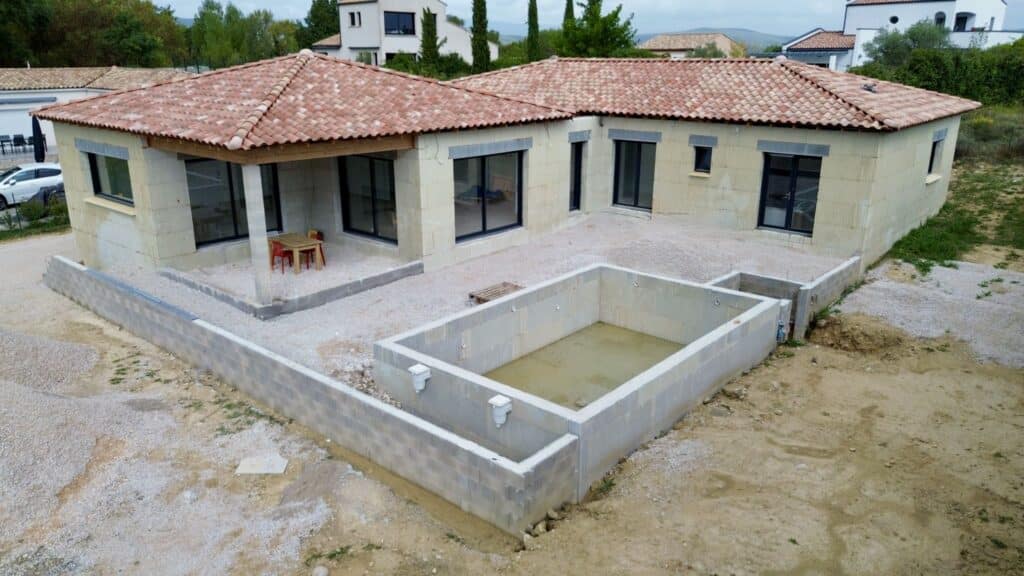 Construction d'une villa moderne avec piscine enterrée en béton, toiture en tuiles et murs isolants extérieurs.