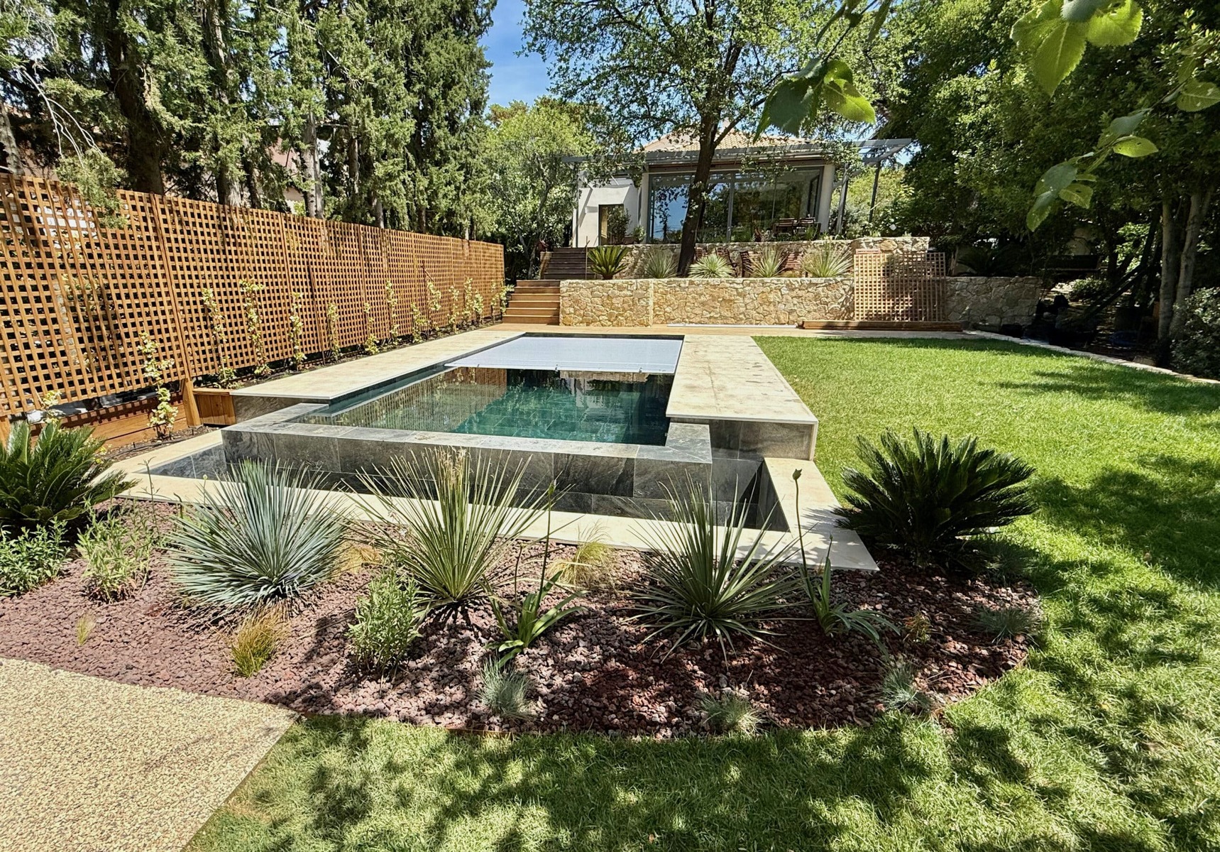 Piscine moderne, terrasse en pierre et jardin paysager avec plantes grasses et pelouse.